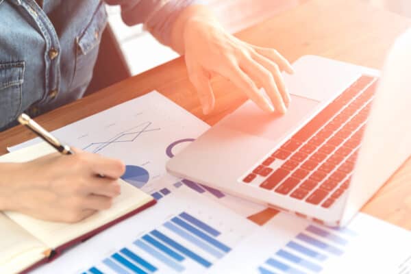 Business,finance and banking concept. Close up of people hand writing on document and typing notebook on wooden table.